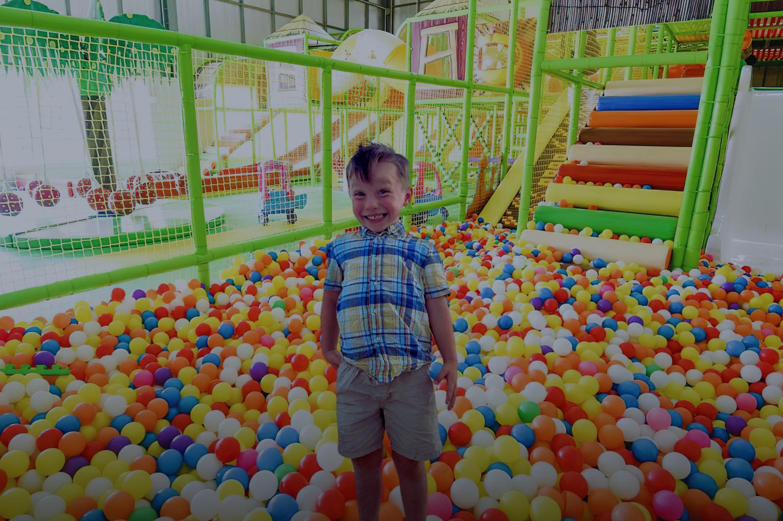 A young child standing in a colorful ball pit in the toddler play area